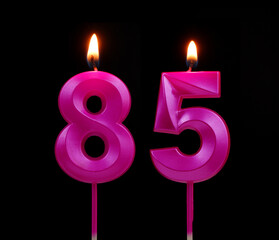 Burning pink birthday candles isolated on black background, number 85.