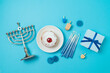 Jewish holiday Hanukkah top view composition with menorah, traditional donuts and gift box on blue background. Flat lay