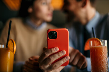 Wall Mural - A businessman and businesswoman are using a smartphone while having a coffee break together in a cafe. Focus on hands