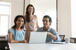 © fizkes - Happy confident diverse employees meeting at shared laptop at workplace, looking at camera, smiling. Business portrait on young multiethnic colleagues, businesspeople, professionals working together