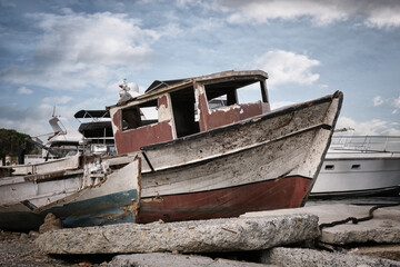 Naklejka na meble An old broken wooden fishing boat against the background of modern yachts.