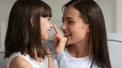 Close up head shot smiling young mother touching little daughter nose with finger, having fun together, family enjoying tender moment, loving mum playing with cute little girl preschool child