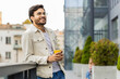 © Andrii Iemelianenko - Happy young Indian man enjoying morning coffee hot drink and smiling outdoors. Relaxing, taking a break. Arabian Hindu guy in urban city downtown street, drinking coffee to go. Town lifestyles outside