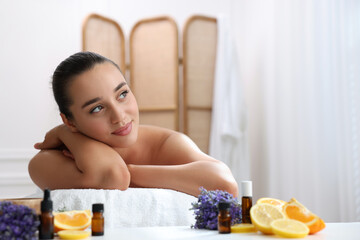 Poster - Beautiful young woman relaxing on massage couch and bottles of essential oil with ingredients on table in spa salon