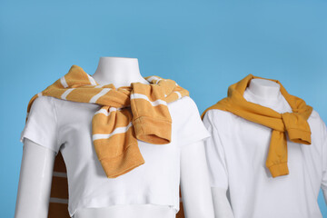 Wall Mural - Female and male mannequins dressed in white t-shirts and orange sweaters on light blue background