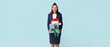 Beautiful stewardess with Santa hat and gift on light blue background