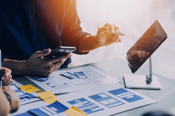 Close up ux developer and ui designer brainstorming about mobile app interface wireframe design on table with customer breif and color code at modern office.Creative digital development agency