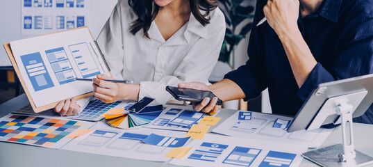 Close up ux developer and ui designer brainstorming about mobile app interface wireframe design on table with customer breif and color code at modern office.Creative digital development agency