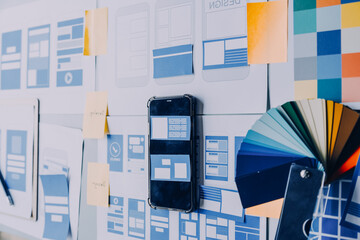 Close up ux developer and ui designer brainstorming about mobile app interface wireframe design on table with customer breif and color code at modern office.Creative digital development agency