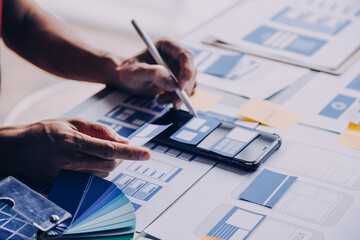 Close up ux developer and ui designer brainstorming about mobile app interface wireframe design on table with customer breif and color code at modern office.Creative digital development agency