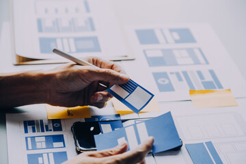 Close up ux developer and ui designer brainstorming about mobile app interface wireframe design on table with customer breif and color code at modern office.Creative digital development agency