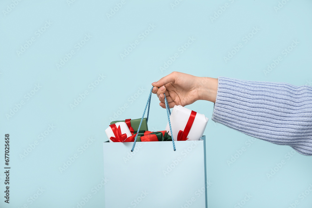 Woman holding shopping bag with Christmas gift boxes on blue background