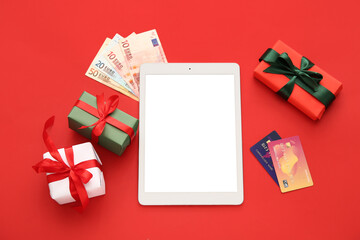 Wall Mural - Modern tablet computer with money, credit cards and Christmas gift boxes on red background