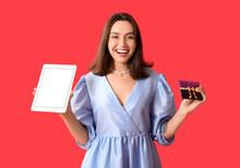Young Woman With Modern Tablet Computer And Gift Card On Red Background. Online Shopping