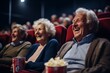 Elderly gray-haired man and woman, with popcorn in their hands, laugh at a movie in the cinema,