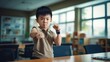 Portrait: Asian funny boy child showing his hand biceps muscles.in the classroom.