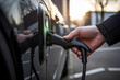 Close-up view of a driver's hand plugging in an electric car charger at a public charging station, on a background of sunset. Selective focus, shallow depth of field