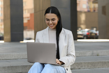 Poster - Happy young woman using modern laptop on stairs outdoors