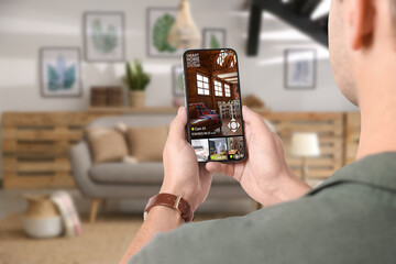 man using smart home security system on mobile phone indoors, closeup. device showing different room