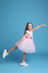 Wall Mural - Cute little girl in beautiful dress dancing on light blue background