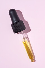 Wall Mural - Bottle pipette dropper and Liquid yellow-orange retinol or vitamin c gel or serum on pink background