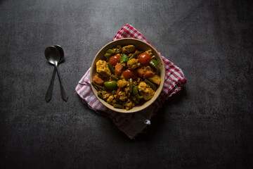 Indian main course dish mixed veg curry prepared with carrots, cauliflower, beans, capsicum and paneer or cottage cheese served in a bowl. Top view, selective focus.