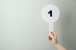 © New Africa - Woman holding auction paddle with number 1 on light grey background, closeup. Space for text