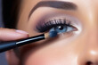 A close-up of a woman's eye applying eyeshadow with a brush. Makeup featuring groomed eyebrows, false eyelashes, and colored contacts. A concept suitable for cosmetics, makeup, and beauty.