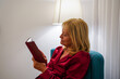 World book day. Mature woman reading an e-book in the electronic tablet on pajamas in room. Sant Jordi tradition with technology