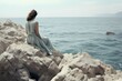 © wpw - A woman in a flowing blue dress sits on white rocks, gazing out at the sea, lost in tranquil thoughts.
