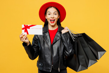 Wall Mural - Young surprised woman wear casual clothes red hat hold shopping paper package bags gift certificate coupon voucher card for store isolated on plain yellow background Black Friday sale buy day concept