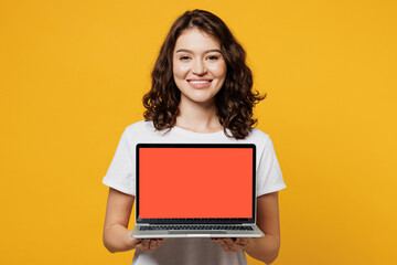 Wall Mural - Young IT woman wears white blank t-shirt casual clothes hold use work on blank screen workspace area laptop pc computer isolated on plain yellow orange background studio portrait. Lifestyle concept.