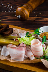 Canvas Print - Fresh slices of bacon, pickles, garlic croutons, lettuce, French mustard and herbs on a wooden board.