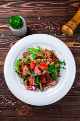 Wall Mural - Meat salad with cherry tomatoes, beef, cucumbers, sun-dried tomatoes, lettuce, arugula and green peas.