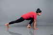 © Anupam - Healthy young woman in red t-shirt and black leggings doing yoga and stretching exercises isolated on grey background