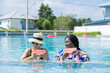 © Rakchanok - Two freelance friends wearing bikinis swimwear and hats with eyeglasses eating tropical fruit watermelon while sunbathing, healthy African and Hispanic females happy relaxing summer holiday vacation
