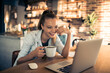 Leinwandbild Motiv Smiling young woman with coffee cup sitting at desk with laptop