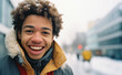 A smiling mixed race black teen standing child in the city square at nigh with a lit up Christmas tree and people, in the background, winter season, snow, happy holidays