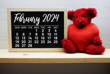 February 2024 Monthly Calendar With Red Teddy Bear And Heart On Wooden Background