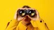 © idaline! - female hands hold black binoculars on a bright yellow background