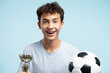 Portrait attractive teenager football player with dental braces holding trophy cup and soccer ball