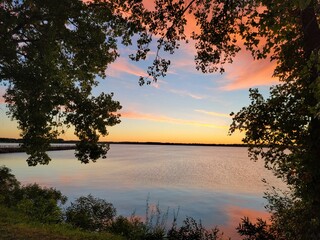 Sticker - Beautiful view of a calm lake lake surrounded by green vegetation during the purple sunset