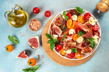 Wall Mural - Fresh Salad with mozzarella, figs, prosciutto, fresh basil leaves and tomato on a light background top view