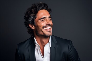 Portrait of a handsome young man laughing against a dark background.