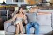 © JackF - Cheerful young woman with husband sitting on sofa in furniture salon, testing softness of cushions and examining quality of upholstery while choosing new furnishings for home..
