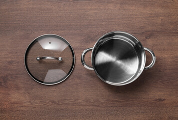 Steel pot and glass lid on wooden table, flat lay