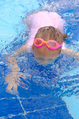 Wall Mural - Child diving in swimming pool. Toddler kid jumping into the water in goggles learning to swim. Girl having fun in water, making bubbles in aquapark