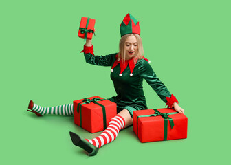 beautiful young woman in elf costume with christmas gift boxes on green background