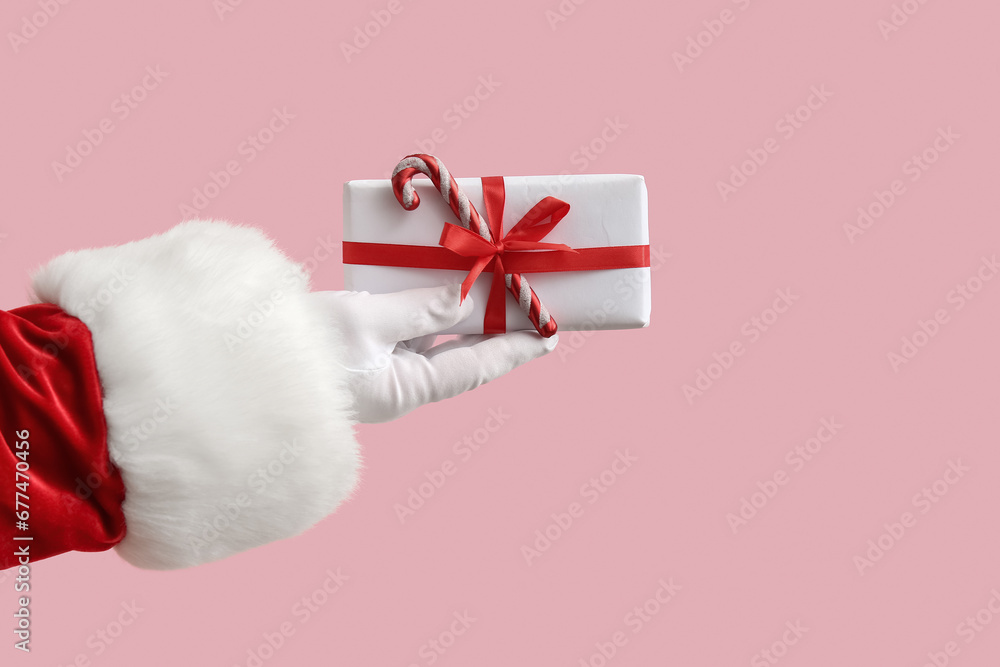 Santa Claus with gift box and candy cane on pink background