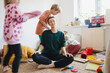 Stressed out mother sitting on floor while children running around her.